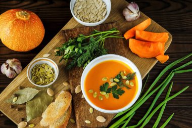 Hafif bir arka planda tohumlar ve otlarla süslenmiş beyaz bir kasede vejetaryen balkabağı kreması çorbası.