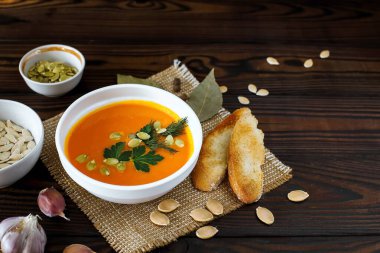 Hafif bir arka planda tohumlar ve otlarla süslenmiş beyaz bir kasede vejetaryen balkabağı kreması çorbası.