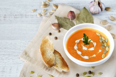 Hafif bir arka planda tohumlar ve otlarla süslenmiş beyaz bir kasede vejetaryen balkabağı kreması çorbası.