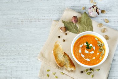 Hafif bir arka planda tohumlar ve otlarla süslenmiş beyaz bir kasede vejetaryen balkabağı kreması çorbası.