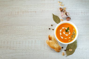 Hafif bir arka planda tohumlar ve otlarla süslenmiş beyaz bir kasede vejetaryen balkabağı kreması çorbası.