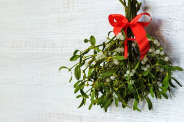 Beyaz arka planda kırmızı kurdeleyle bağlanmış böğürtlenli sonsuz yeşil ökseotu dalları. Noel konsepti