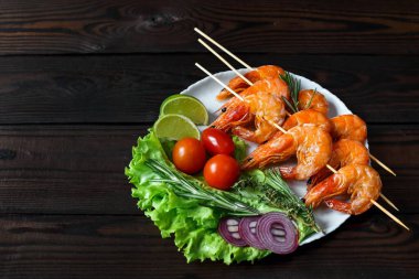 Arka planda sebze ve otlarla dolu bir tabakta ızgara karides. Şiş ızgara karides, restoran menüsü, Akdeniz mutfağı.