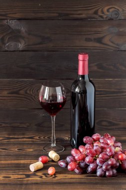 Bir bardak ve bir şişe kırmızı şarap. Koyu ahşap bir masada olgun üzümler. metin için alanı olan dikey yerleşim
