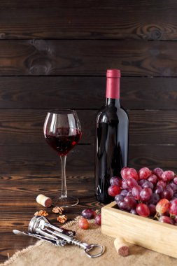 Bir bardak ve bir şişe kırmızı şarap. Koyu ahşap bir masanın üzerindeki bir kutuda olgunlaşmış üzümler. Tex için alanı olan dikey yerleşim