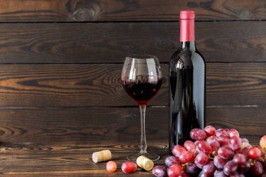 Bir bardak ve bir şişe kırmızı şarap. Koyu ahşap bir masada olgun üzümler. yatay yerleşim 