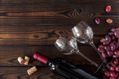 Bardakların üst görüntüsü ve bir şişe kırmızı şarap. Koyu ahşap bir masada olgun üzümler. Metin için alanı olan yatay yerleşim
