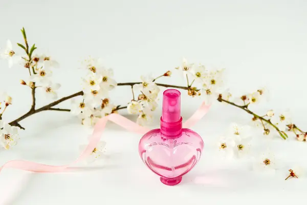 香水装在瓶子里 以心脏的形式出现在开花枝干的背景上 妇女香水 — 图库照片