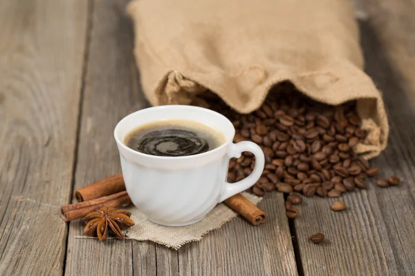 Saco de café cheio de grãos de café e xícara branca de café na frente — Fotografia de Stock