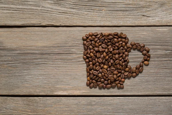 Granos de café colocados en forma de una pequeña taza sobre un fondo de madera — Foto de Stock