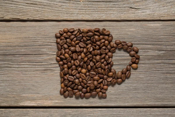 Grains de café placés sous la forme d'une grande tasse sur une table en bois — Photo