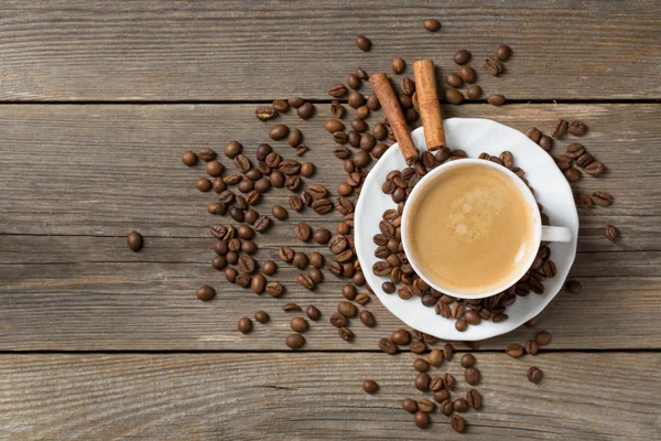 Taza de café con palitos de canela y granos de café colocados en una mesa de madera —  Fotos de Stock