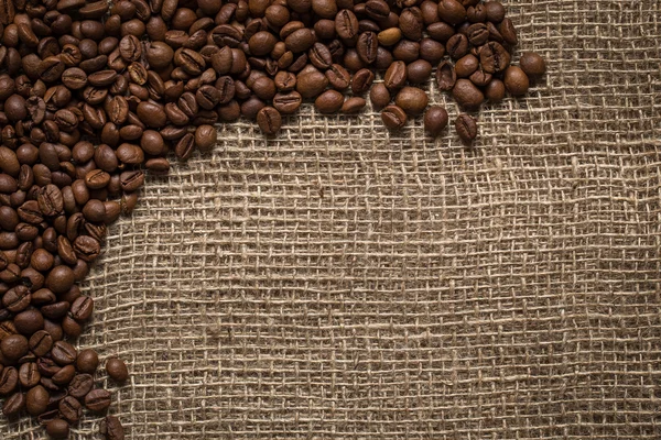 Рассеянные кофейные зерна на фоне мешковины — стоковое фото