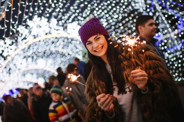 De mooie jongedame die bij de kerstmarkt staat met sprankelingen in haar handen — Stockfoto