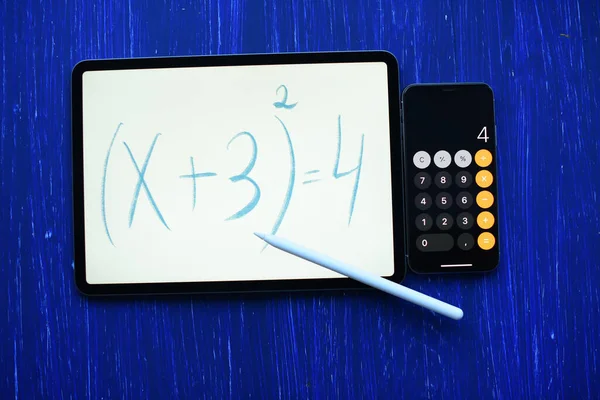 Tablet with the mathematical equation inscription with Pencil and phone -calculator on blue background