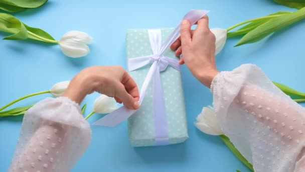 Mujeres abre regalo .Girl unbox regalo con cinta blanca en azul y tulipanes floridos background.Close arriba.. — Vídeo de stock