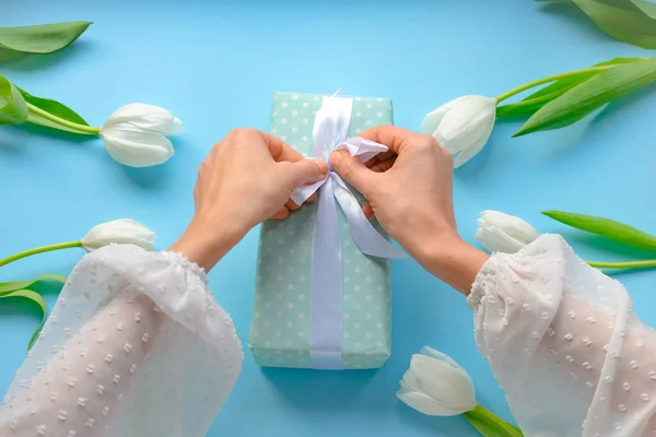 women opens gift .Girl unbox present with white ribbon on blue and flowery tulips packing present gift. Packing gift present. Close up.Top view.