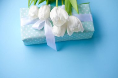 Hediye ve çiçekler mavi arka planda beyaz laleler. Kadınlar günü. Anneler Günü. Çiçekler. Beyaz kurdeleli bir hediye..