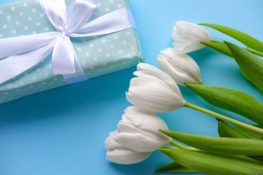 Hediye ve çiçekler mavi arka planda beyaz laleler. Kadınlar günü. Anneler Günü. Çiçekler. Beyaz kurdeleli bir hediye..