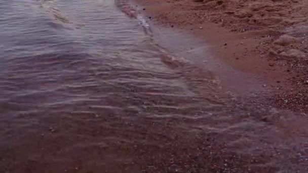 Textura de la superficie del agua, ondulaciones y olas, textura de arena del lado del mar rojo, puesta del sol brillan fondo de agua. Playa roja y arena — Vídeo de stock