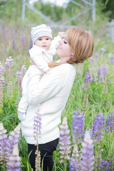 Young mother with baby at meadow lupins flowers — Stock Photo, Image