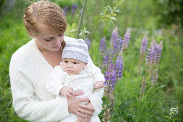 Young mother with baby at meadow lupins flowers — Stock Photo, Image