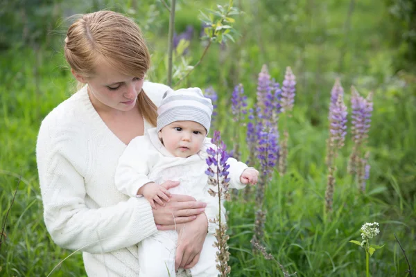 Young mother with baby at meadow lupins flowers — Stock Photo, Image