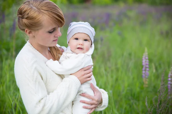 Young mother with baby at meadow lupins flowers — Stock Photo, Image