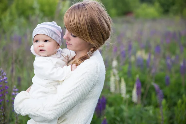 Young mother with baby at meadow lupins flowers — Stock Photo, Image