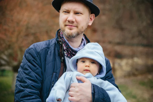 Батько обіймає маленького сина надворі. Носіння капелюха і куртки — стокове фото