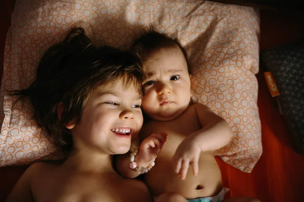 Girl and baby lying together on the pillow. Playing and smiling — Stock Photo, Image