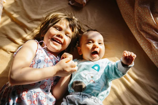 Mädchen und Baby liegen zusammen auf dem Bett. Spielen und lächeln — Stockfoto