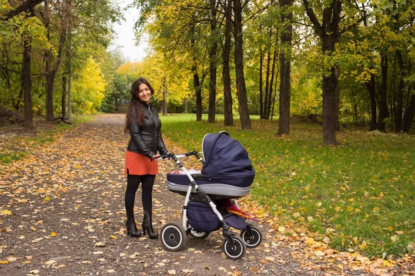 Young smiling mum walks with pram in the aurumn yellow park — Stock Photo, Image