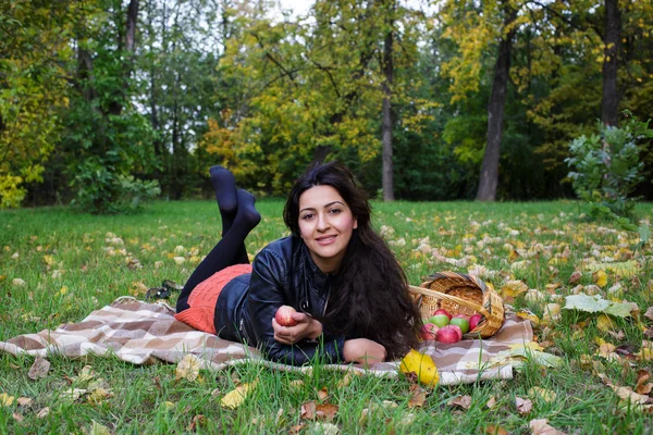 Ung kvinna ligger på en filt på gräset i höst park och leenden — Stockfoto