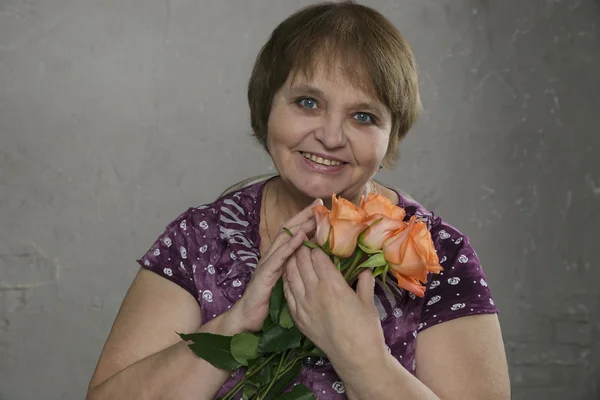 Närbild porträtt av glad äldre kvinna med blommor tittar på kameran och ler — Stockfoto