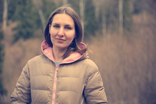 Happy young woman in jacket standing over spring forest trees. P