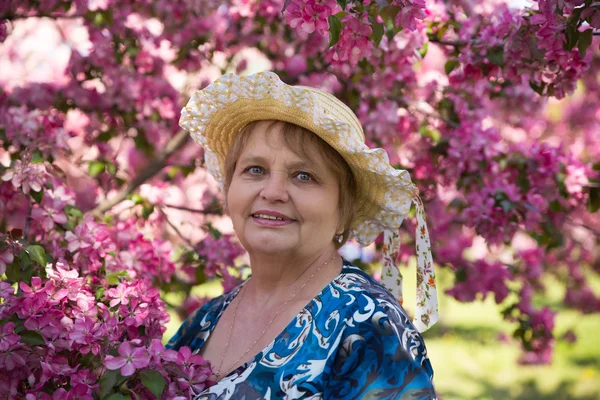 Feliz mujer mayor bajo flores rosadas en verano — Foto de Stock