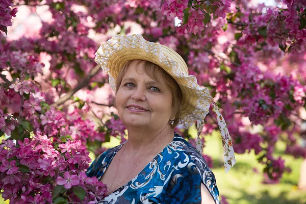 Mujer adulta en sombrero bajo flores rosas árboles — Foto de Stock