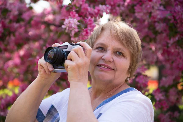 Portrait of woman with camera under pink flowers in summer — Stock Photo, Image