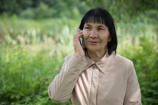 Telefonla yaz yeşil zemin üzerine kıdemli Çuvaş bilen bir kadın — Stok fotoğraf