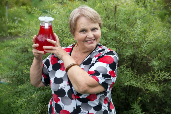 Smiling senior woman showing jug with fresh stewed fruit — Stock Photo, Image