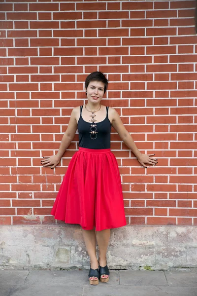 Ung kvinna som bär röd kjol nära vägg — Stockfoto