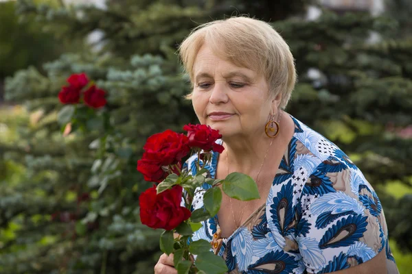 Pensionär kvinna med rosor i trädgården Stockbild