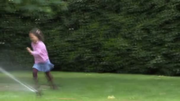 Девушка бежит через разбрызгиватель — стоковое видео