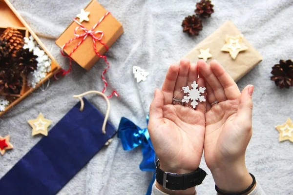 Snowflake in hands. Gift wrapping process. Blue bow. Gifts in craft paper. Festive atmosphere. New Year's decor. Minimalistic gift wrapping