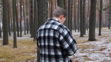 Dalgın bir adam ormanda duruyor. Ekose gömlekli taşralı adam. Renkli kış ormanı