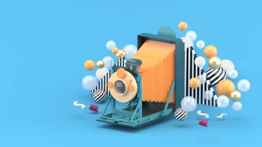 Eski kamera mavi arka planda renkli topların arasında yüzüyor.