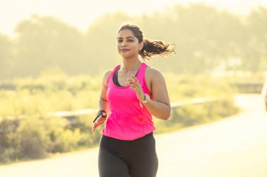 Yürüyüş yolunda koşan bir kadın, parlak pembe spor kıyafetleri giyiyor.