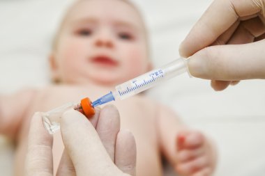 Doktor bebeği aşılamak için şırınga tutar