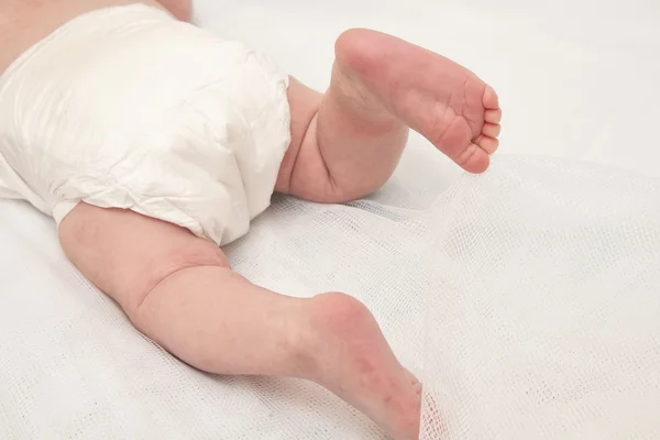 Pies de un bebé de dos meses con pañales acostados en la cama en casa —  Fotos de Stock